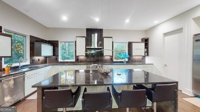 kitchen with wall chimney exhaust hood, premium appliances, backsplash, and a sink