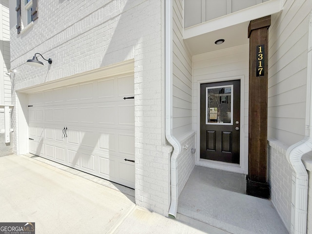 doorway to property with a garage, brick siding, and concrete driveway