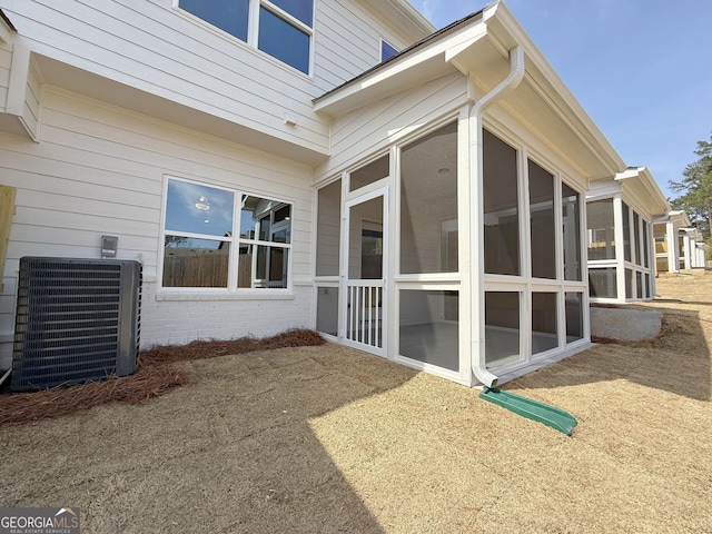 view of home's exterior with central AC unit, brick siding, and a sunroom