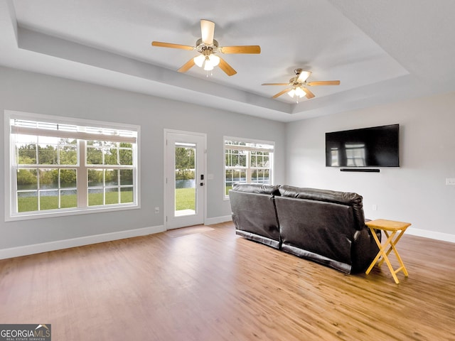 living room with light wood-type flooring, a tray ceiling, and ceiling fan