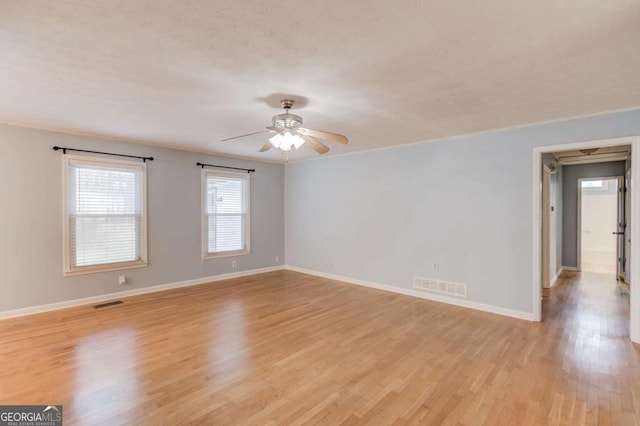 empty room with light wood-style flooring, a ceiling fan, visible vents, and baseboards