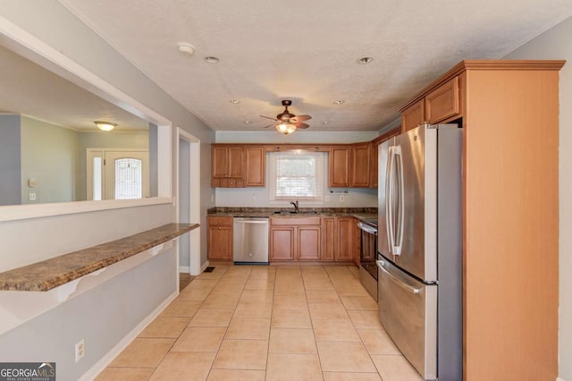 kitchen featuring brown cabinetry, a ceiling fan, stainless steel appliances, a sink, and light tile patterned flooring