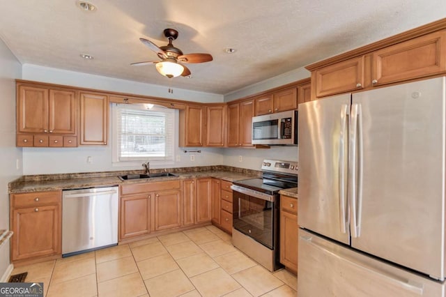 kitchen with light tile patterned floors, ceiling fan, a sink, appliances with stainless steel finishes, and brown cabinetry