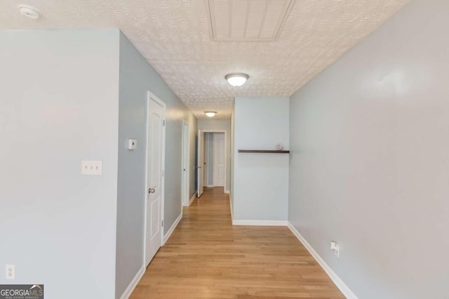 hallway featuring a textured ceiling, light wood-style flooring, visible vents, and baseboards