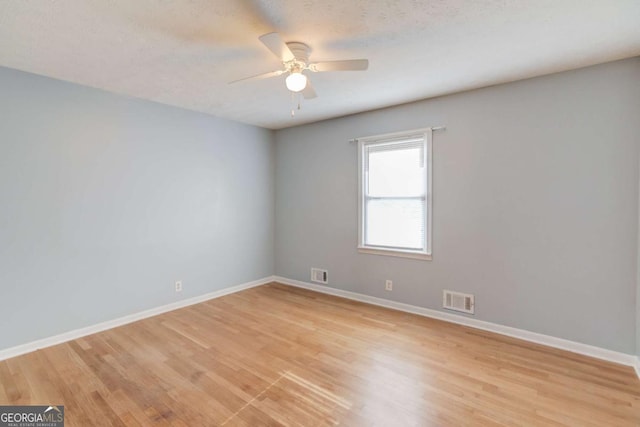 empty room featuring light wood finished floors, a ceiling fan, visible vents, and baseboards