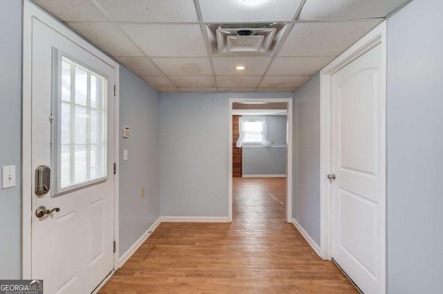 doorway with baseboards, a drop ceiling, and light wood-style floors