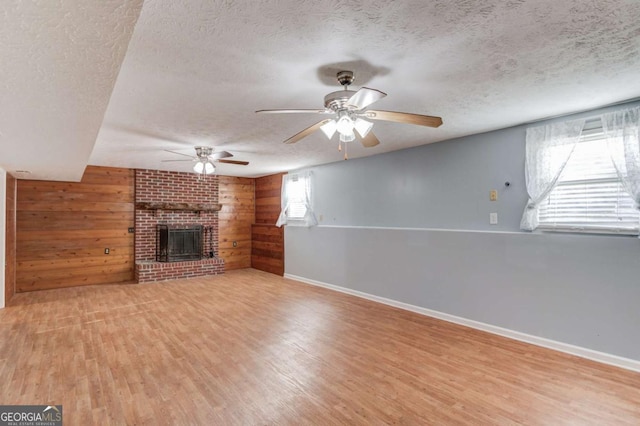 unfurnished living room with a brick fireplace, wooden walls, a textured ceiling, and wood finished floors