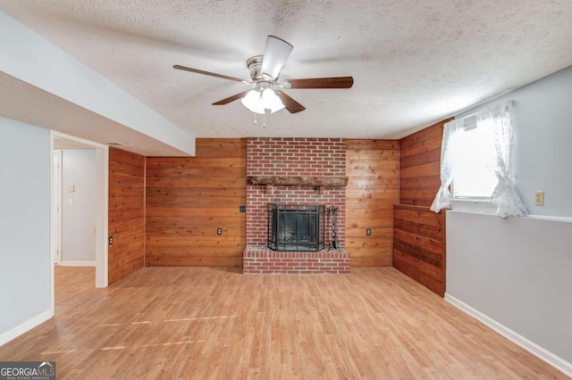 unfurnished living room with wood walls, a fireplace, wood finished floors, and a textured ceiling