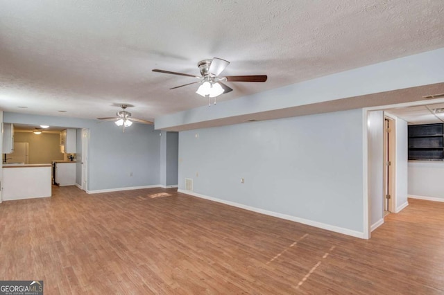 unfurnished living room with a ceiling fan, a textured ceiling, baseboards, and wood finished floors