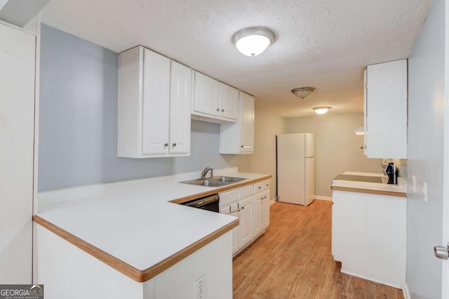 kitchen featuring light countertops, freestanding refrigerator, white cabinets, a sink, and a peninsula