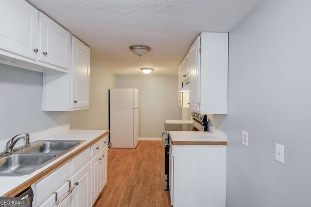 kitchen with electric range, white cabinets, a sink, and freestanding refrigerator