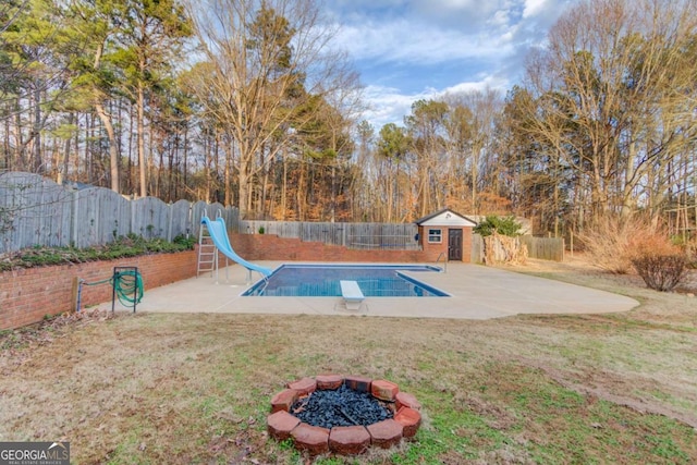 view of pool with a fire pit, a fenced backyard, a water slide, a yard, and an outdoor structure