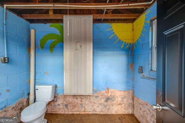 bathroom with toilet and concrete block wall