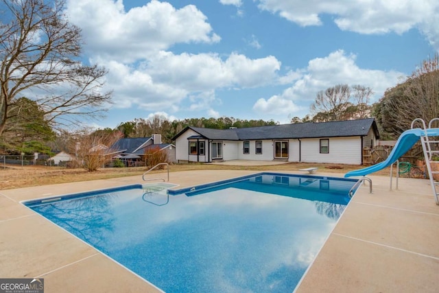 pool with a patio area, fence, a diving board, and a water slide