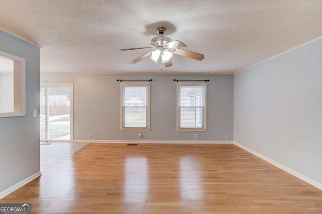 empty room with ornamental molding, baseboards, light wood-style flooring, and a textured ceiling