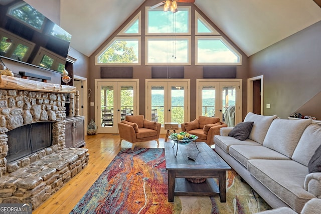 living room featuring a stone fireplace, a healthy amount of sunlight, light wood-type flooring, and french doors