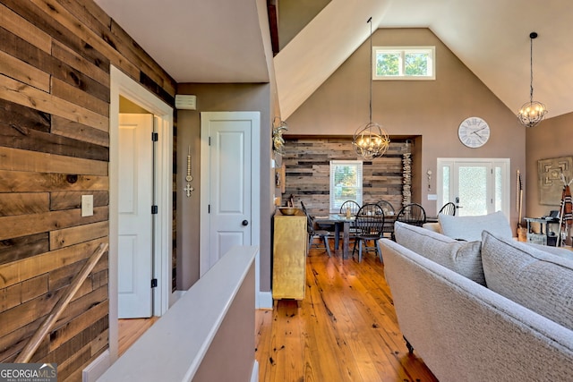 hall featuring light hardwood / wood-style flooring, high vaulted ceiling, a chandelier, and wood walls