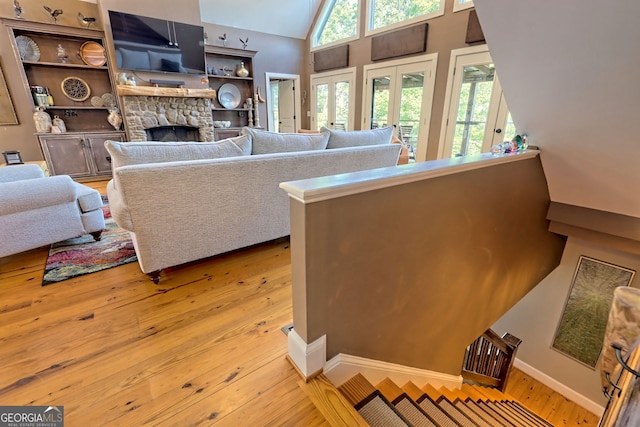 living room with a stone fireplace, high vaulted ceiling, light hardwood / wood-style floors, and french doors