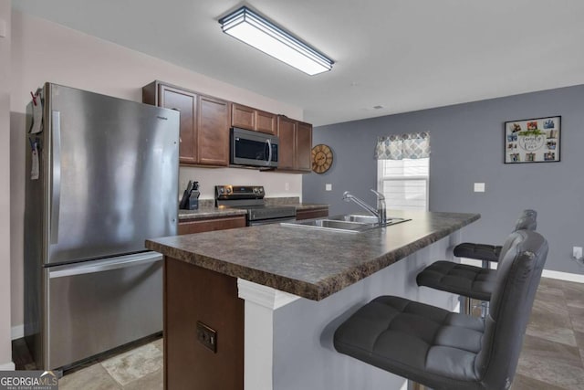 kitchen with dark brown cabinetry, sink, a breakfast bar area, appliances with stainless steel finishes, and kitchen peninsula