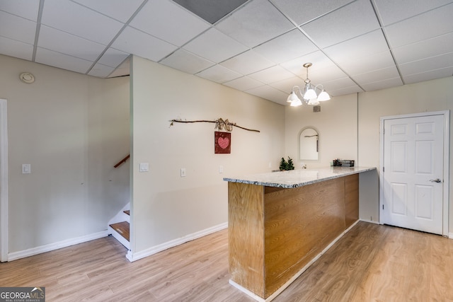 bar with light stone counters, a paneled ceiling, hanging light fixtures, light hardwood / wood-style flooring, and a notable chandelier