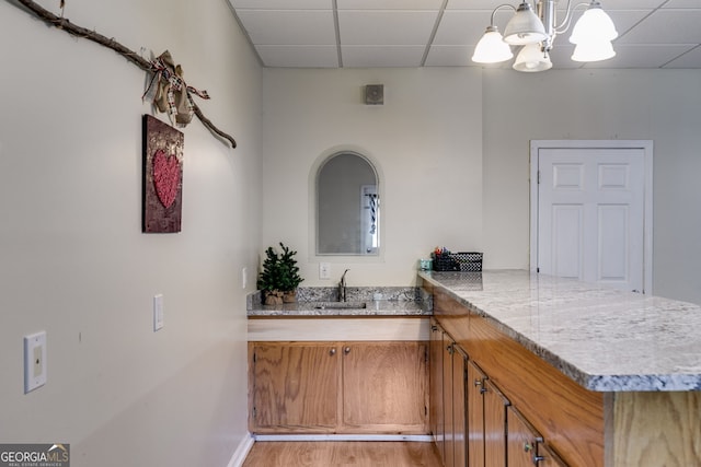 interior space with sink, a notable chandelier, kitchen peninsula, a drop ceiling, and light hardwood / wood-style flooring