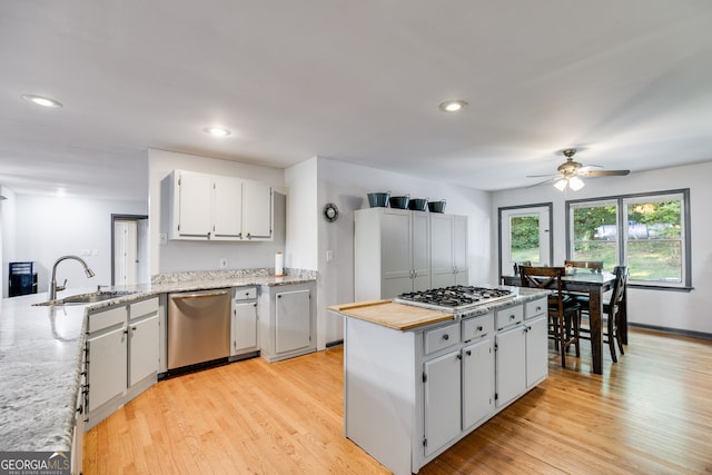 kitchen with sink, light wood-type flooring, appliances with stainless steel finishes, ceiling fan, and light stone countertops