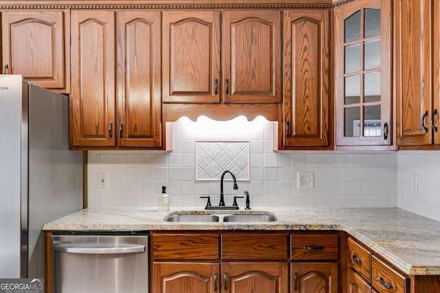 kitchen featuring tasteful backsplash, stainless steel appliances, light stone countertops, and sink