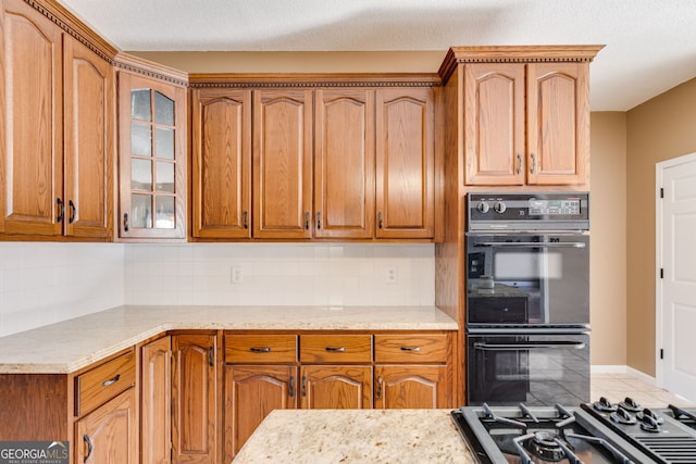 kitchen featuring light stone counters, a textured ceiling, gas cooktop, black double oven, and backsplash