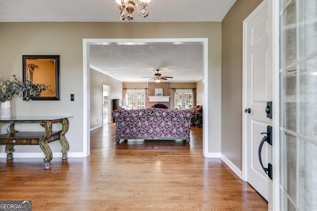 interior space with wood-type flooring, a brick fireplace, a textured ceiling, ornamental molding, and ceiling fan with notable chandelier