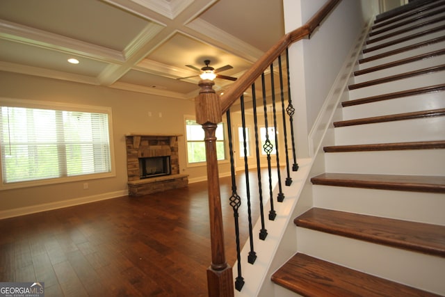 stairs featuring hardwood / wood-style flooring, crown molding, coffered ceiling, a stone fireplace, and beamed ceiling