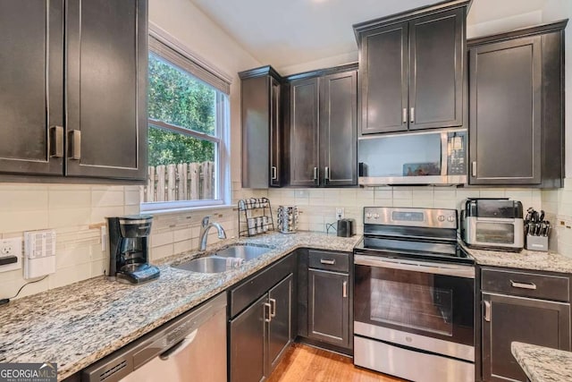 kitchen with appliances with stainless steel finishes, sink, decorative backsplash, light stone countertops, and light wood-type flooring