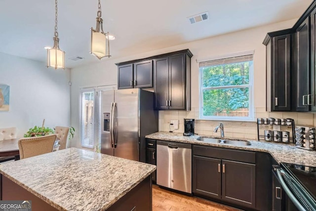 kitchen featuring decorative light fixtures, sink, decorative backsplash, a center island, and stainless steel appliances