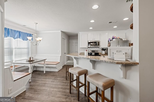 kitchen with appliances with stainless steel finishes, white cabinetry, light stone counters, breakfast area, and decorative light fixtures