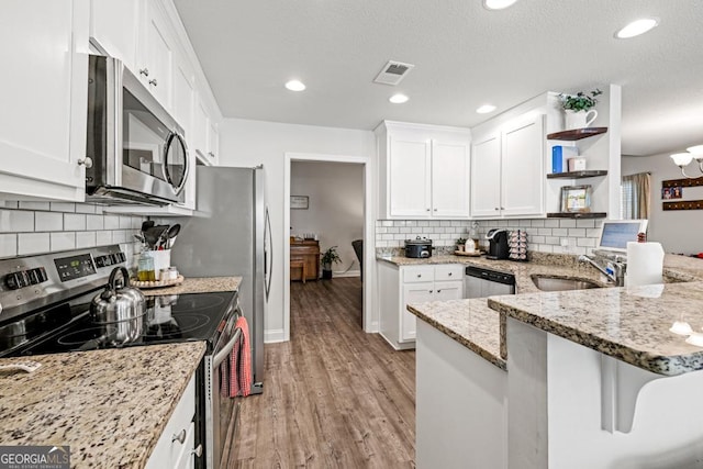 kitchen featuring light stone countertops, kitchen peninsula, white cabinets, and appliances with stainless steel finishes