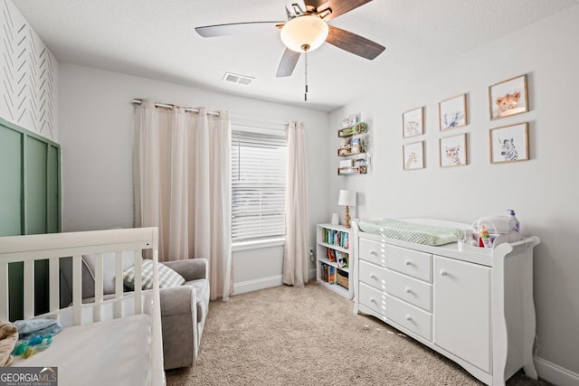 carpeted bedroom featuring a nursery area and ceiling fan