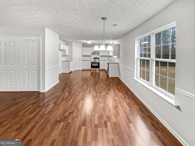 unfurnished dining area with an inviting chandelier, sink, dark hardwood / wood-style floors, and a textured ceiling