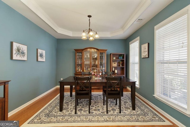 dining area featuring ornamental molding, a tray ceiling, a chandelier, and wood-type flooring