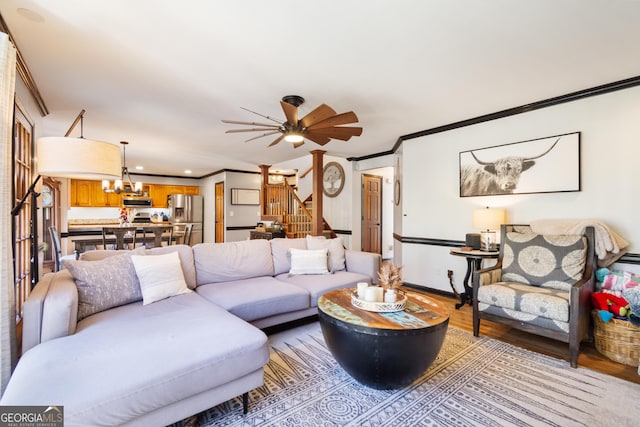 living room with ceiling fan with notable chandelier, crown molding, and light hardwood / wood-style flooring