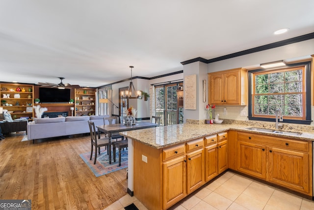 kitchen with sink, decorative light fixtures, kitchen peninsula, light stone countertops, and ornamental molding