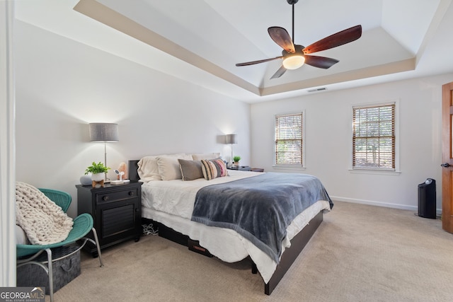 bedroom with light carpet, ceiling fan, and a tray ceiling