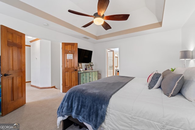 bedroom featuring ensuite bath, light colored carpet, ceiling fan, and a raised ceiling