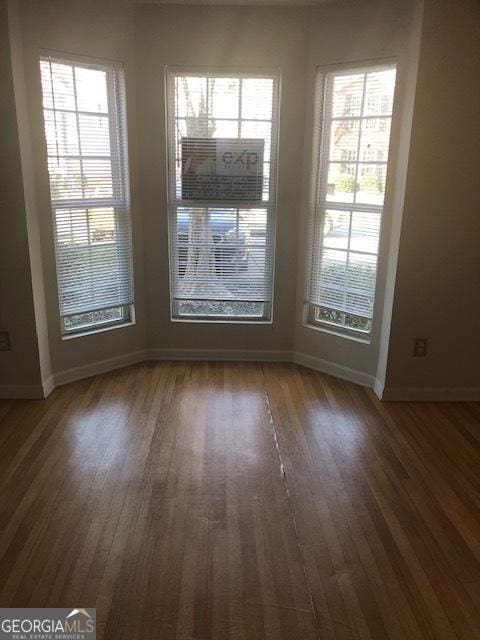 empty room featuring a wealth of natural light, dark wood-style flooring, and baseboards