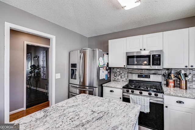 kitchen with stainless steel appliances, white cabinets, and light stone counters