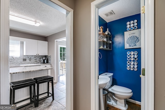 bathroom featuring a textured ceiling, sink, toilet, and tasteful backsplash