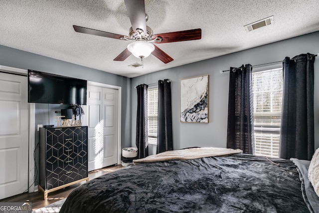 bedroom with ceiling fan, multiple windows, a textured ceiling, and hardwood / wood-style floors