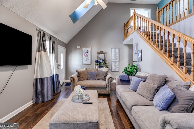 living room with ceiling fan, a high ceiling, dark hardwood / wood-style floors, and a skylight