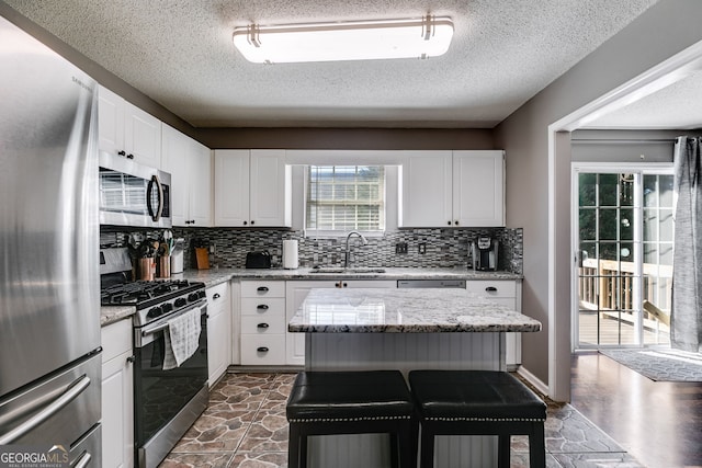 kitchen with appliances with stainless steel finishes, sink, white cabinetry, and light stone countertops