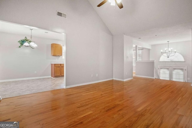 unfurnished living room with high vaulted ceiling, ceiling fan with notable chandelier, and light wood-type flooring