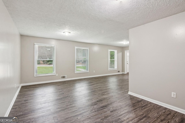 spare room with dark wood-type flooring, visible vents, a textured ceiling, and baseboards