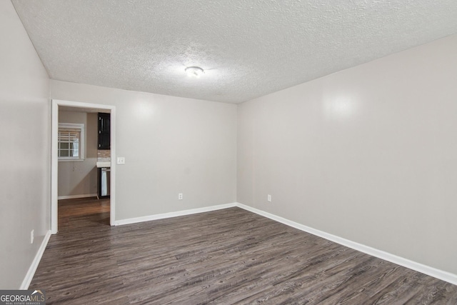 spare room featuring a textured ceiling, dark wood-type flooring, and baseboards